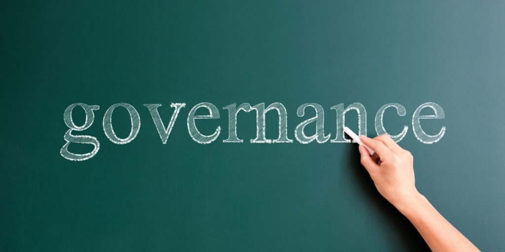 A hand holding a chalk writing on a board the word "governance"